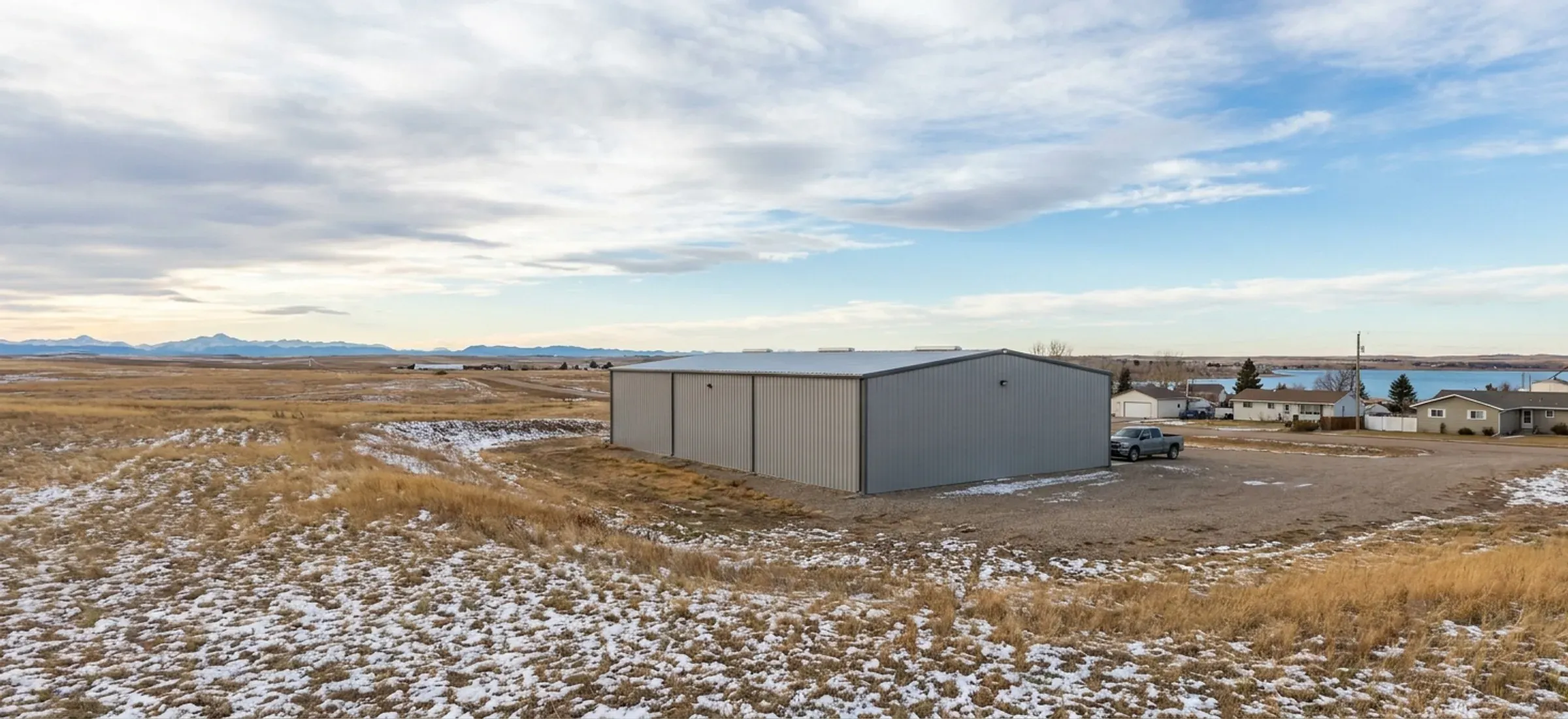 A steel commercial building on flat land near a lake, with low prairie and open sky behind